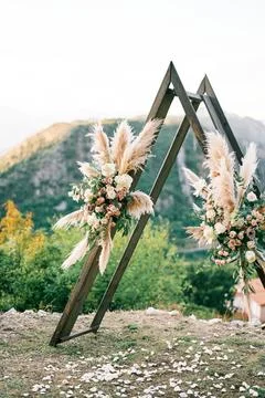 Triangular wedding tipi arch decorated with flowers stands on a mountain Stock Photos