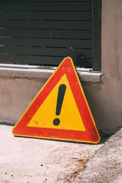 Triangular yellow and red road warning sign with an exclamation mark leanin.. Fotos Stock