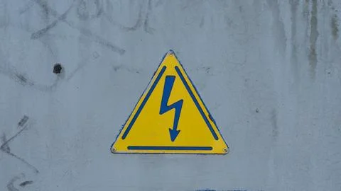 A triangular yellow high voltage warning sign with a blue lightning bolt symb Stock Photos