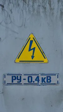 A triangular yellow high voltage warning sign and an industrial plate with Ru Stock Photos