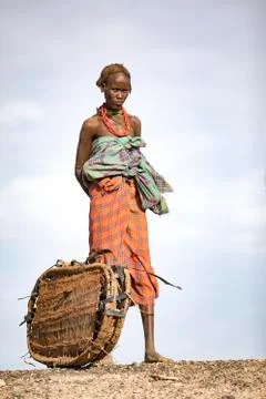 A tribal lady from Ethiopia stands watching with a basket next to her. Stock Photos