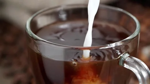 Trickle of fresh milk pouring into glass mug of coffee near bag of roasted beans Stock Footage 146869341
