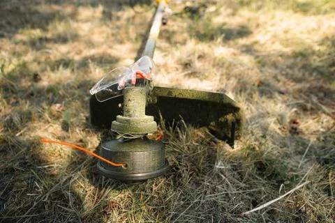 Trimmer after mowing grass close-up. Petrol pump on the grass with safety gla Foto stock