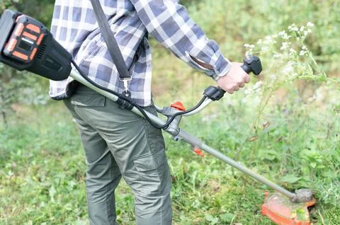 Trimming the Green: A person using a string trimmer with a shoulder strap, .. Photos