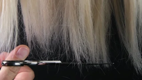 Trimming split ends of unkempt blonde hair with scissors on a black background Stock Footage 321223067