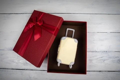 Trip as a gift concept. red gift box with miniature travel suitcase Stock Photos