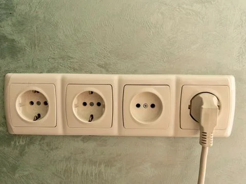 Triple electrical outlet with plug on textured wall. Close-up of a triple w.. 스톡 사진