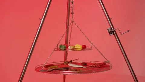 Tripod Swing Grill Holding Vegetables and Sausages, Red Background, Studio Shot Stock Footage 341515037