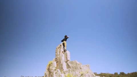 Triumphant Climber Celebrating on Mountain Summit Against Clear Blue Sky Stock Footage 271224344