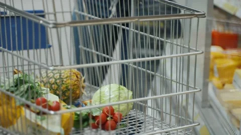 A trolley filled with groceries standing in the rows of a supermarket. Video stock 237455728