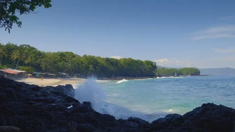 Tropical beach with big waves and white splashes on black rock with many people Stock Footage 114689645