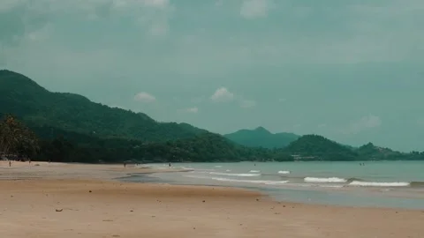Tropical beach with calm waves, sandy shore, and lush green mountains Stock Footage 282082386