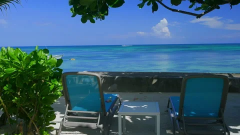 Tropical beach lounge chairs overlooking turquoise ocean horizon Stock Footage 346367962