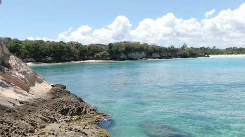 Tropical beach, massive rocky cliffs and blue water, sunny day, foamy waves, 4k Stock Footage 154803781