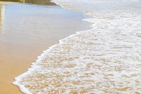 Tropical beach sand texture with clear waves and reflective ocean surface T.. Stock Photos