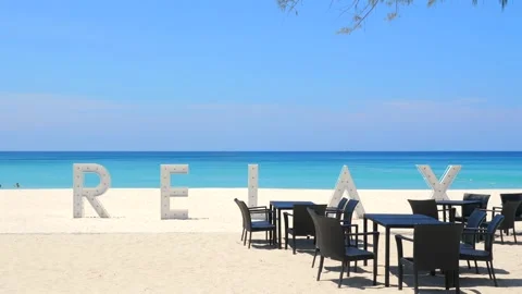 Tropical beachfront cafe setting with large 'RELAX' sign on pristine Stock Footage 264466090