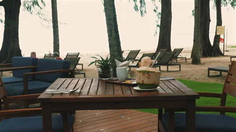 Tropical beachside cafe with wooden table, coconut drink, and lounge Video stock 282082542