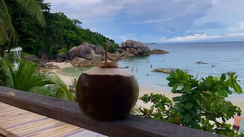 Tropical coconut drink with a straw on the background of a golden beach and sea Stockbeeldmateriaal 243270835