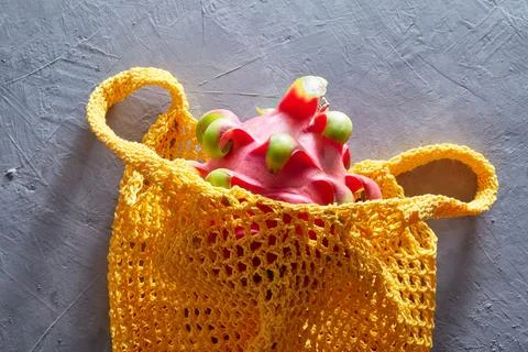 Tropical Dragon fruit in a string bag on a gray concrete background. Shopping Fotos Stock