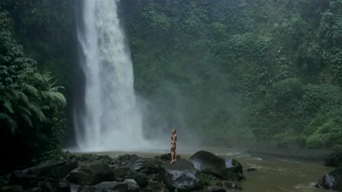 Tropical powerful waterfall in the depth of Bali jungle. Woman tourist posing Stock Footage 238668706