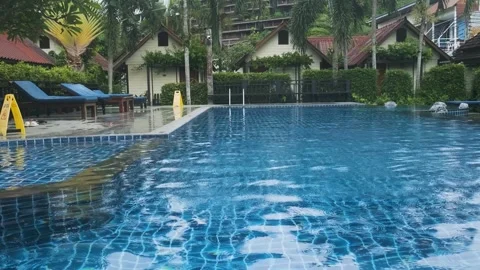 Tropical resort swimming pool with clear blue water, surrounded by lush greenery Stock Footage 288111593