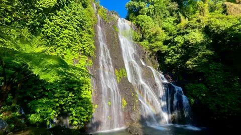 Tropical Waterfall Cascading Down Cliff with Rainbow in Bali Foto stock