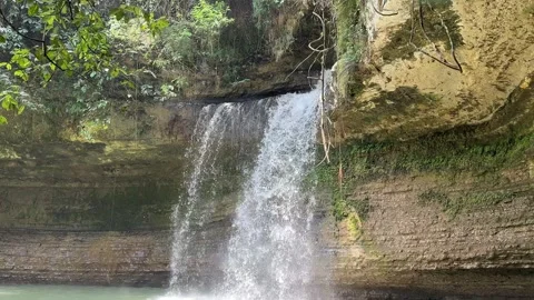 Tropical Waterfall Cascading Down Rock Cliff into Natural Pool Stock Footage 325646612