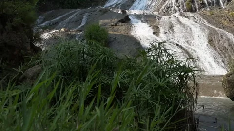 Tropical Waterfall Cascading Over Rocks, Green Foliage, Revealing Shot Video stock 325646033