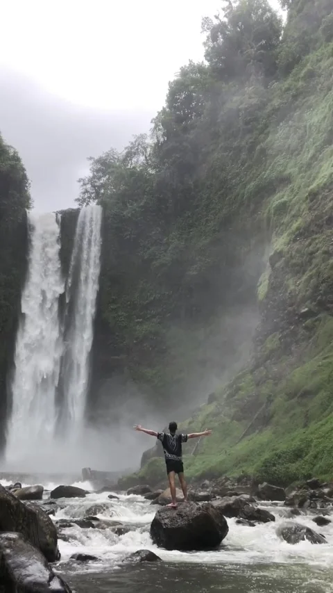 Tropical Waterfall &amp; a man standing in front of it, Indonesia. Видео 343605716