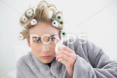 Troubled blonde woman in hair curlers crying and using tissues Stock Photos