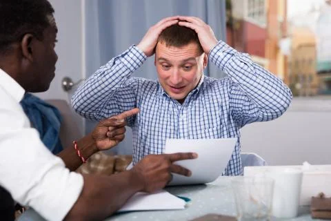 Troubled man discussing documents with partner at home Stock Photos