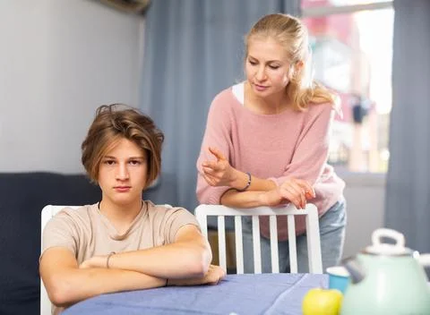 Troubled teen boy sitting at home while his mother scolding him Stock Photos