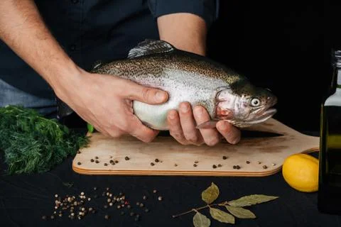 Trout in hands of a man on background of kitchen. Big fresh fish with chef Stock Photos