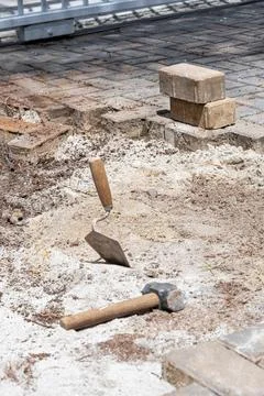 A trowel in the sand next to a small mallet and concrete blocks on a sunny .. Stock Photos