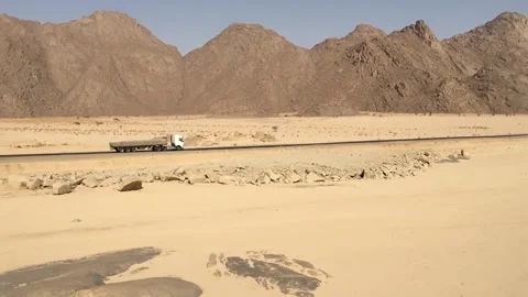 A truck driving in the depths of the desert between mountains and sand Stock Footage