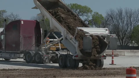 Truck dumps load of dirt as Interstate traffic moves in background, 4K. Stock Footage 151592623
