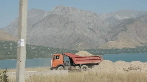 Truck throws sand against the backdrop of mountains and a lake, Uzbekistan Stock Footage 246703208