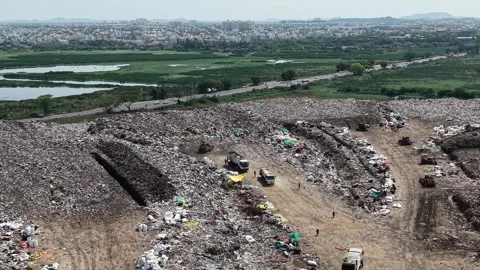 Trucks Arriving To Dump Waste On Cleared Land Beside Green Fields Stockbeeldmateriaal 341465960