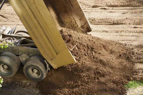 The truck's bed tips to release a load of soil, close-up,  earth pouring out  Stock Photos
