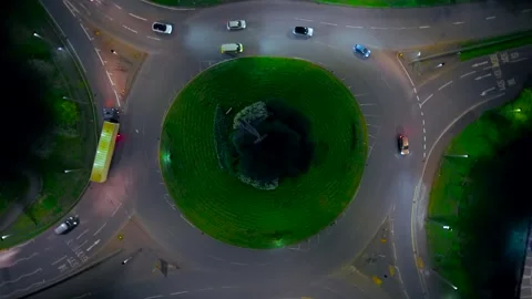 Trucks driving through illuminated roundabout at night with cars moving along Stock Footage 336543670