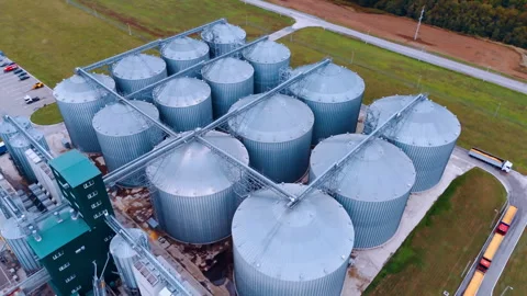 Trucks loaded with grain stand around the group of huge metal tanks.  Stock Footage 298669723
