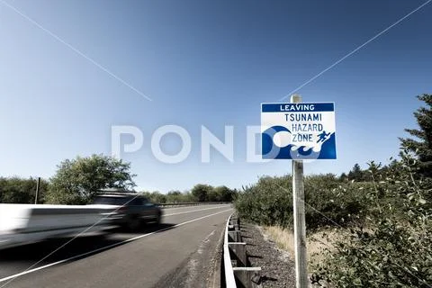 A tsunami warning sign along a coastal highway with a blurred car passing by Stock Photos