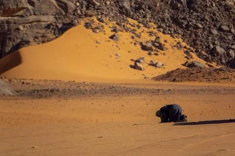 Tuareg man kneeling in prayer on a sand dune in the desert, Tassili N'Ajjer.. 스톡 사진
