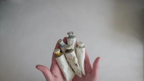 Tubes of paint are held in their hands, then placed on a white table Stock Footage 169835157