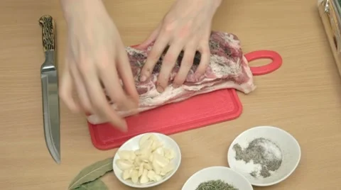 Tucking thin slices of garlic in salted and peppered bacon. Stock-Footage 7740898