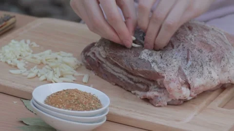 Tucking thin slices of garlic in salted and peppered pork Stock Footage 7766796