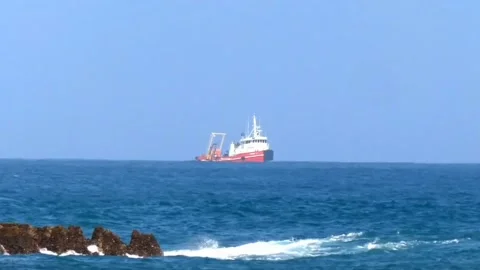 Tug Boat Cargo Ship Far Away on the Sea passing through some crashing Waves Stock Footage 238571367
