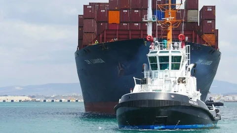 Tug boat in front a large container ship entering a sea port 4k Stock Footage 105462843