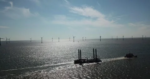 Tug boat towing large load infront of the Scroby Sands Wind Farm Stock Footage 148300752
