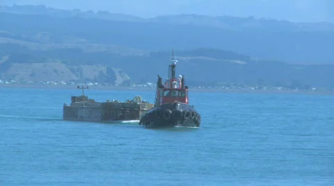 Tug pulling barge through harbor entrance Stock Footage 322371